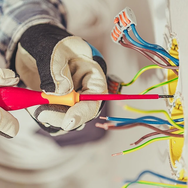 manos de electricista profesional con guantes aprietan tornillo con destornillador en punto de luz